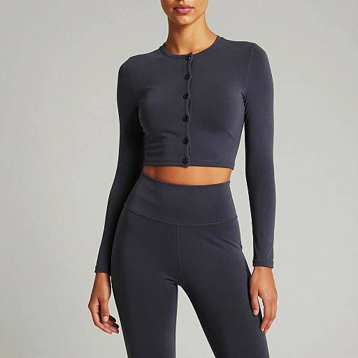 Photograph of a woman with light brown skin wearing a black, long-sleeve, button-up crop top and high-waisted black leggings against