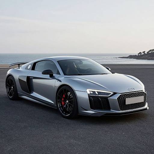 Photograph of a sleek silver Audi R8 sports car with black accents, red brake calipers, and black rims, parked on a coastal road with