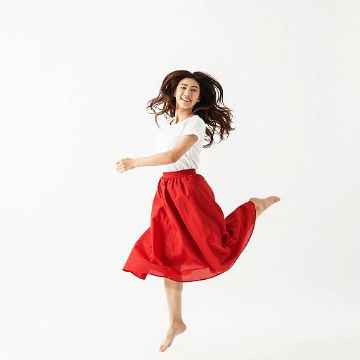 Photograph of a smiling young woman with long black hair, wearing a white top and flowing red skirt, mid-jump against a white background.