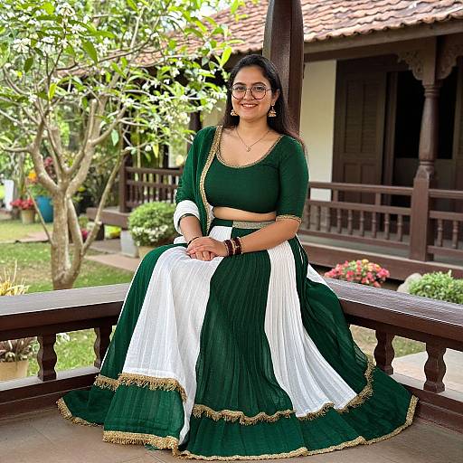Photograph of a smiling Indian woman with medium skin tone, dark hair, and glasses, wearing a green and white traditional lehenga with gold trim,