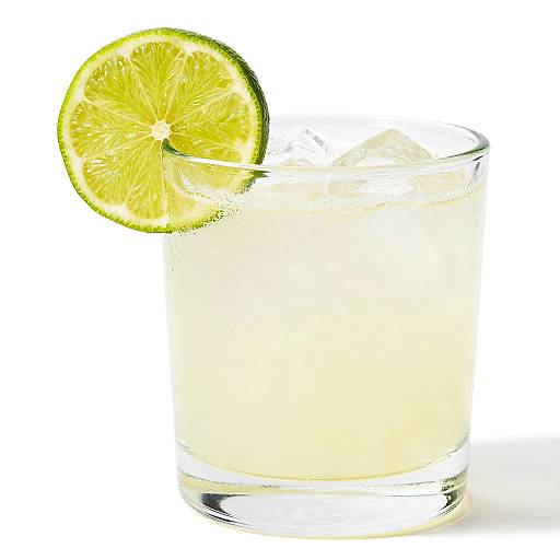 Photograph of a clear glass filled with a pale yellow liquid, garnished with a fresh lime slice on the rim.