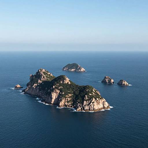 Photograph of a clear blue ocean with several rocky, green-topped islands scattered across the horizon under a bright blue sky.