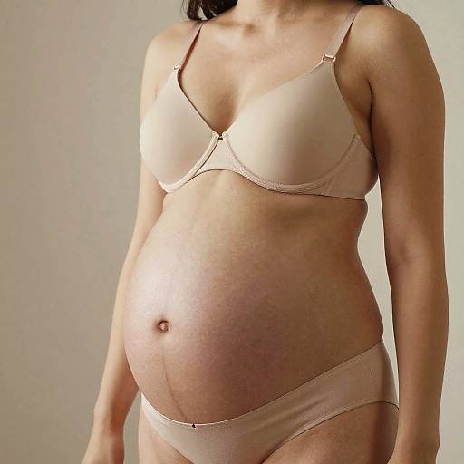 Photograph of a pregnant woman in beige bra and panties, standing against a plain white background, showing her round belly and natural skin tone.
