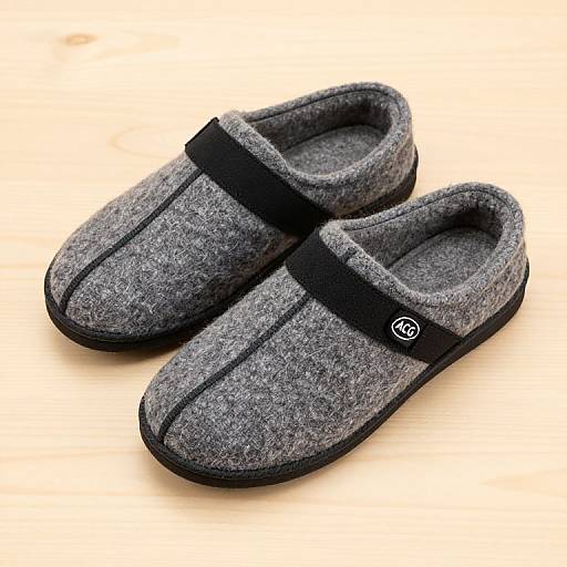 Photograph of gray, woolen slip-on shoes with black straps and black soles, positioned on a light wooden surface.