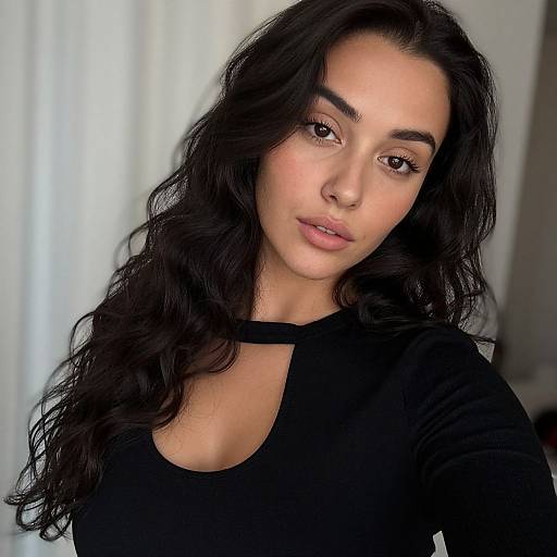 Photograph of a young woman with long, wavy black hair, medium skin tone, and brown eyes, wearing a black top, against a softly