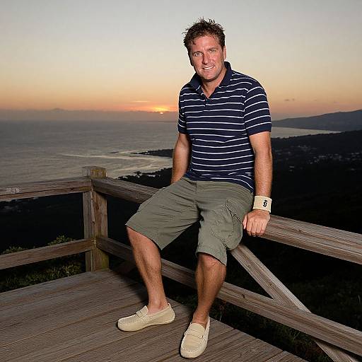 Photograph of a middle-aged man with short, curly brown hair, wearing a navy striped polo, khaki shorts, and beige sneakers, sitting on