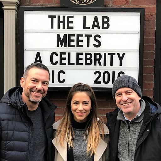 Photograph of three smiling people standing in front of a marquee reading 