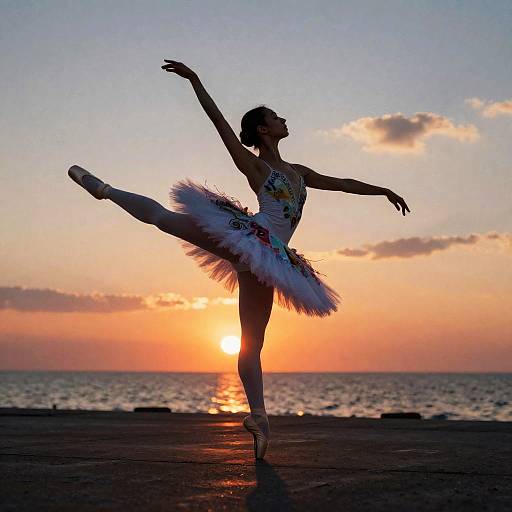 Silhouetted ballerina in tutu performing a high kick at sunset, with a glowing orange and purple sky and calm sea behind. Phot