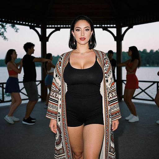Photograph of a curvy woman with medium skin tone, black hair, wearing a black tank top, shorts, and patterned cardigan, standing