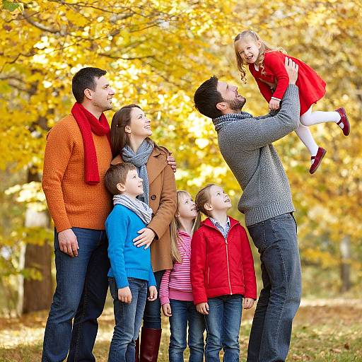 Photograph of a smiling family in autumn, with a father lifting a daughter in a red dress, surrounded by yellow-leaved trees.