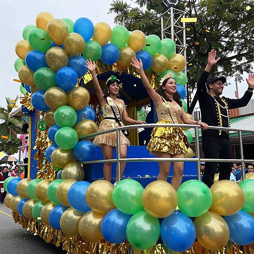 Colorful parade photo: Three women in gold fringe dresses, black outfits, and green headbands, waving, surrounded by blue and gold balloons.