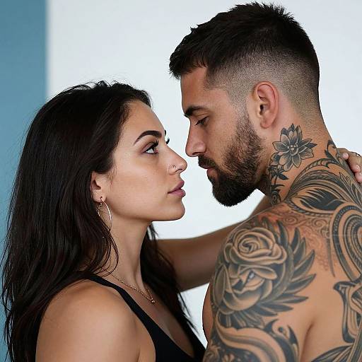Photograph of a tattooed, bearded man with dark hair and a floral neck tattoo, intimately facing a dark-haired woman with nose ring, black