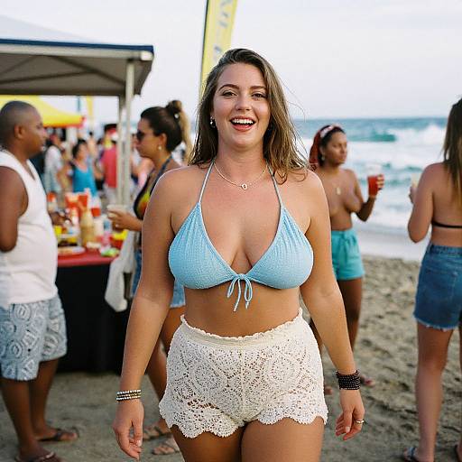 Photograph of a smiling, curvy woman with light brown hair, wearing a blue bikini top and white lace shorts, walking on a bustling beach with