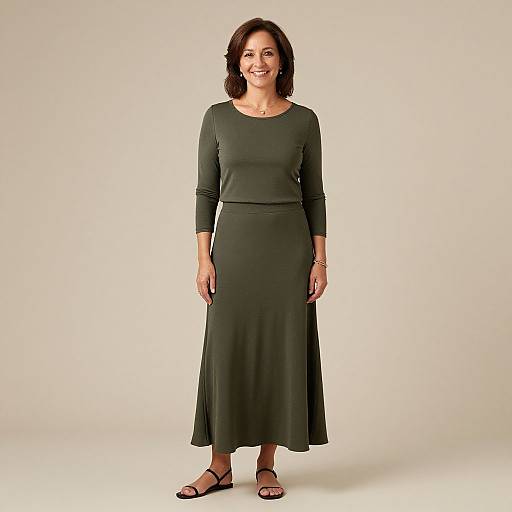 Photograph of smiling middle-aged woman with shoulder-length dark brown hair, wearing a long-sleeve, dark green dress and black sandals, standing against