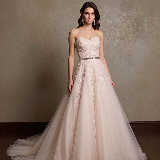 Photograph of a brunette bride in a strapless, white lace and tulle wedding gown, standing against a textured beige wall.