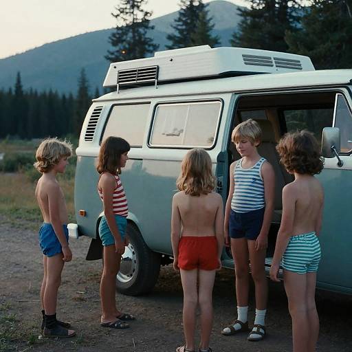 Photograph of six young children in summer shorts and tank tops standing beside a white van with a roof rack in a forest clearing. Mountain background. Casual