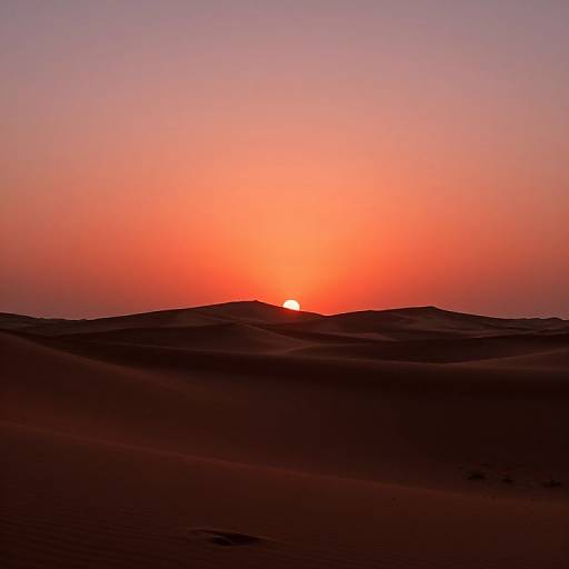 Photograph of a vivid sunset over a desert with rolling sand dunes, silhouetted against a gradient sky of red, orange, and purple
