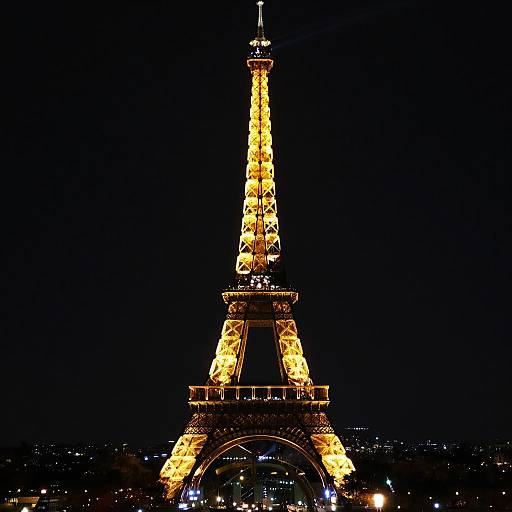 Photograph of the illuminated Eiffel Tower at night, glowing in bright yellow lights against a dark sky, with distant city lights visible at the base