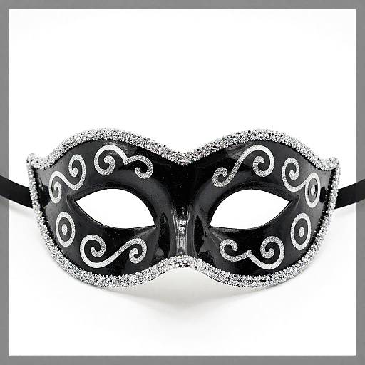 Photograph of a black masquerade mask with white, swirling patterns and glittery edges, set against a white background.