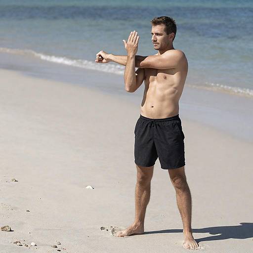 Shirtless Man Stretching on Sandy Beach