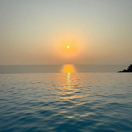 Photograph of a serene sunset over calm ocean water, with the sun casting a golden reflection on the rippling surface.