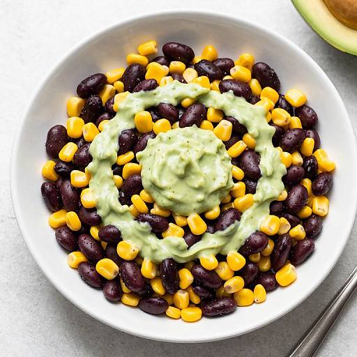 Photograph of a white bowl filled with black beans and yellow corn, topped with a green, creamy sauce.