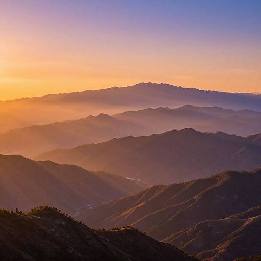 Photograph of a stunning sunrise over layered mountain ranges, with vibrant orange and blue sky gradients, casting soft shadows on dark, silhouetted peaks