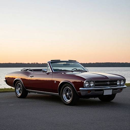 Photograph of a shiny, classic red convertible muscle car with chrome details, parked on an asphalt road by a lake at sunset.