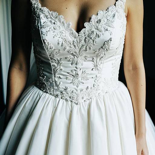Photograph of a woman in a white lace-embellished strapless wedding dress, highlighting the intricate floral lacework on the bodice.