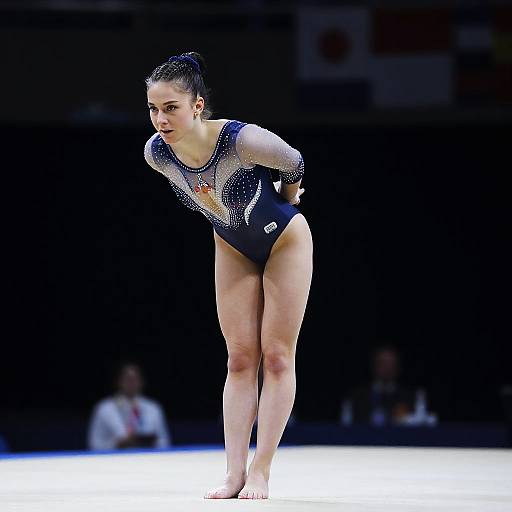 Photograph of a focused female gymnast with dark hair in a bun, wearing a black and silver sparkly leotard, bending forward on a
