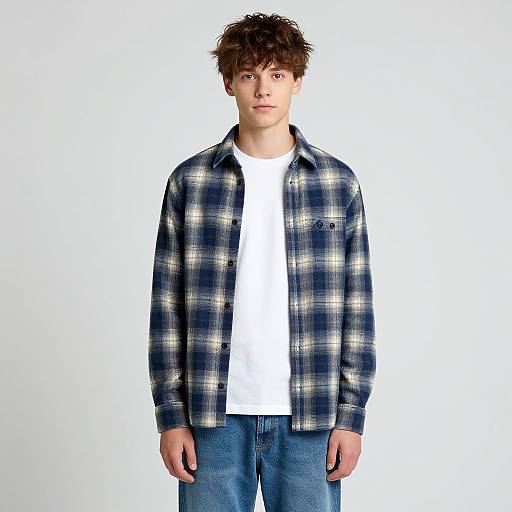 Photograph of a young man with tousled brown hair, wearing a blue and white plaid shirt over a white t-shirt, and blue jeans,