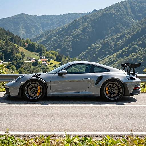 Photograph of a sleek, silver Porsche 911 GT3 with black rims and yellow brake calipers parked on a mountain road, lush green hills and