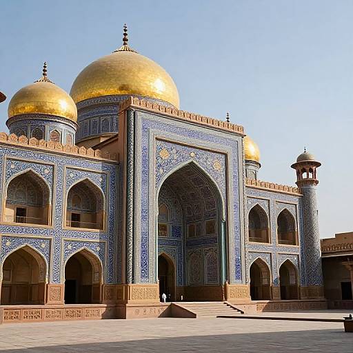 Photograph of a Mughal-style mosque with blue and white tilework, two golden domes, and a tall minaret under a clear blue