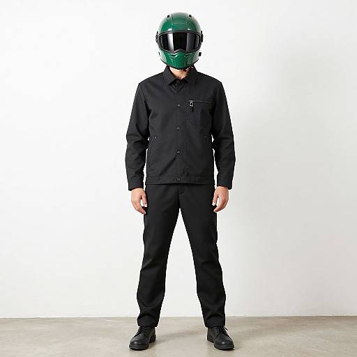 Photograph of a man in black outfit, green helmet with reflective visor, standing against white background, concrete floor.