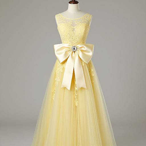 Photograph of a yellow lace dress with a large satin bow, delicate tulle skirt, and a silver brooch at the bow's center.