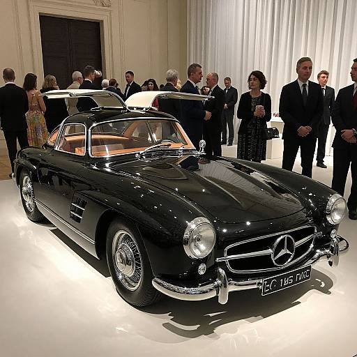 Photograph of a sleek, black vintage Mercedes-Benz convertible on display in an elegant, well-lit gallery, surrounded by formally dressed attendees.
