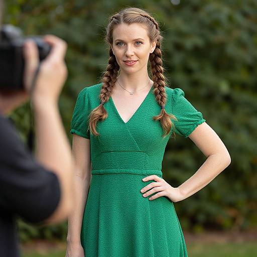 Photograph of a fair-skinned woman with long brown braids, wearing a green dress, standing outdoors with a photographer taking her photo.