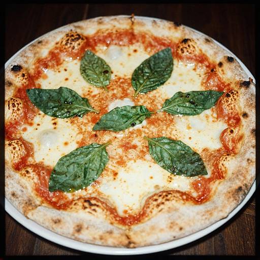 Photograph of a classic Margherita pizza with fresh basil leaves, melted cheese, and a slightly charred, crispy crust on a white plate.