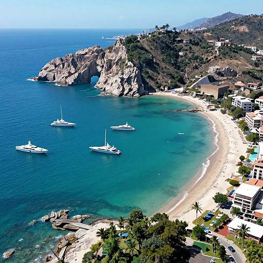 Aerial photograph of a serene coastal scene with turquoise waters, rocky cliffs, three white yachts, sandy beach, lush greenery, and hillside