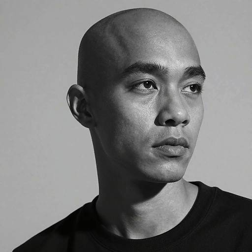 Black-and-white photograph of a bald, light-skinned man with smooth skin, slightly parted lips, and intense gaze, wearing a black shirt, against