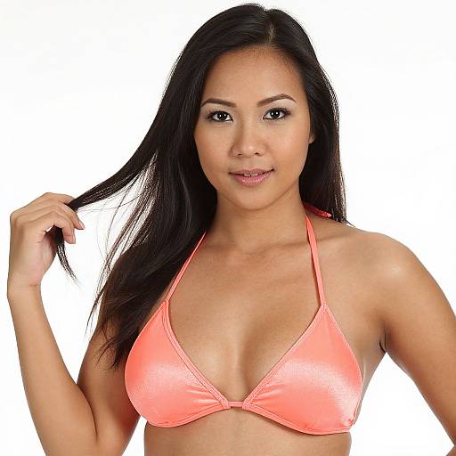 Photograph of an attractive Asian woman with long black hair, wearing a shiny, neon pink bikini top, holding her hair, against a white background.