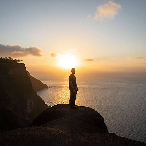 Photograph of a silhouetted person standing on a cliff, gazing at a vibrant sunset over a calm ocean, with dark cliffs on the