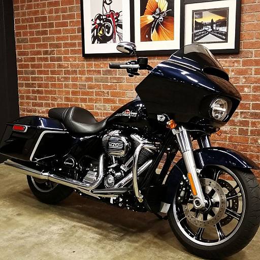 Photograph of a black Harley-Davidson motorcycle with chrome accents, parked against a red brick wall, framed abstract art in background.