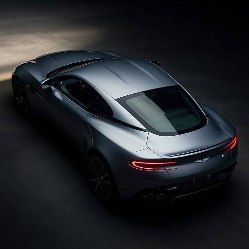Photograph of a sleek, silver Tesla Model S sports car with red taillights, viewed from above in a dark, shadowy setting.