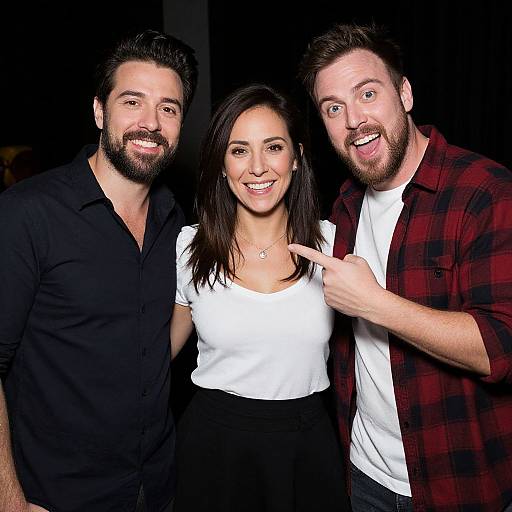 Photograph of three smiling people: bearded man in black shirt, woman in white top and black pants, bearded man in red plaid shirt