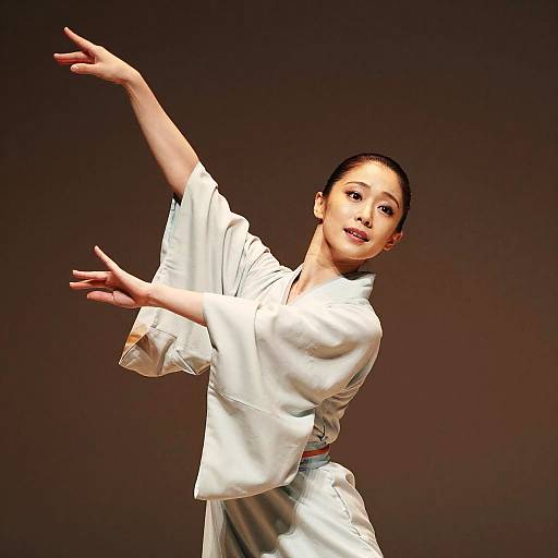 Photograph of an Asian woman in a white martial arts gi, performing a dynamic karate pose against a dark brown background.
