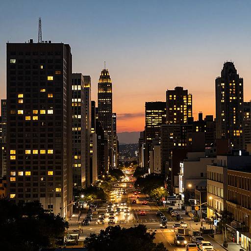 Photograph of a bustling urban street at dusk, with silhouetted skyscrapers, glowing yellow windows, and a vibrant orange-pink sunset
