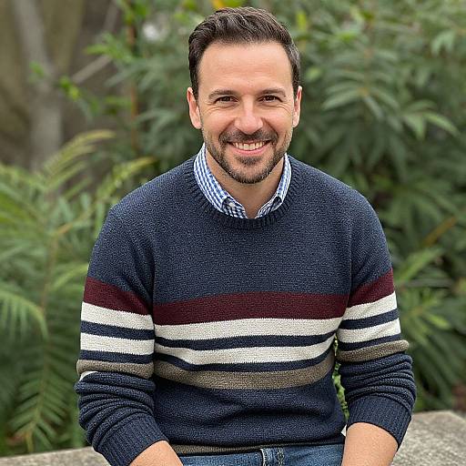 Photograph of a smiling, middle-aged man with short dark hair and beard, wearing a navy and white striped sweater, blue checkered shirt, and