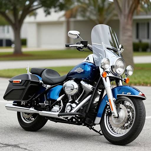 Photograph of a shiny blue Harley-Davidson motorcycle with a clear windshield, black saddlebags, and chrome details, parked on a suburban street.