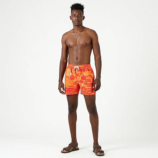 Photograph of a tall, muscular, dark-skinned Black man with short, spiked hair, wearing orange, patterned swim trunks and sandals,